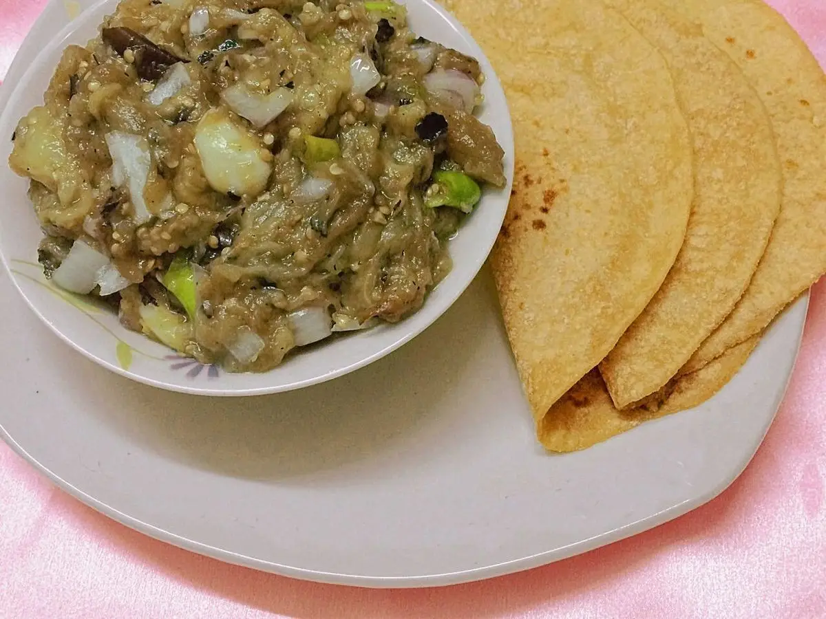Cuenco de berenjena asada y machacada con cebolla junto a panes planos sobre un plato