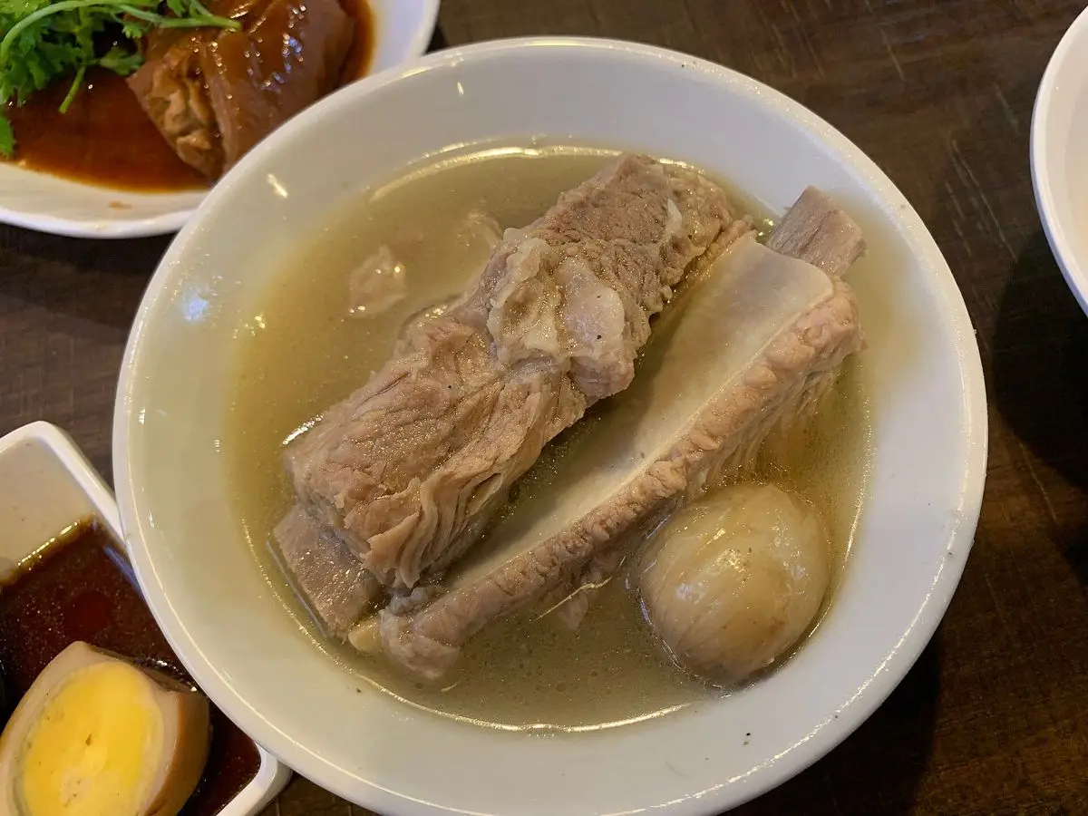 Cuenco de sopa clara de costillas de cerdo con huevo cocido y salsas al lado