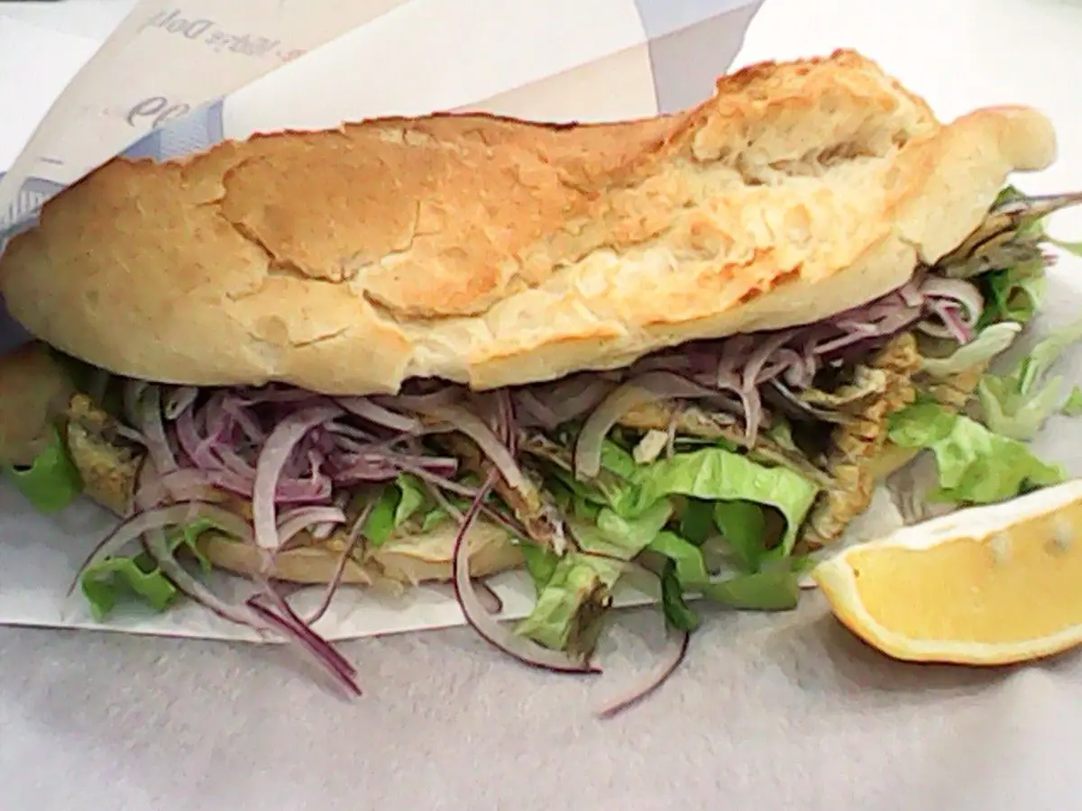 Bocadillo turco de pescado con cebolla morada, lechuga y una cuña de limón sobre papel