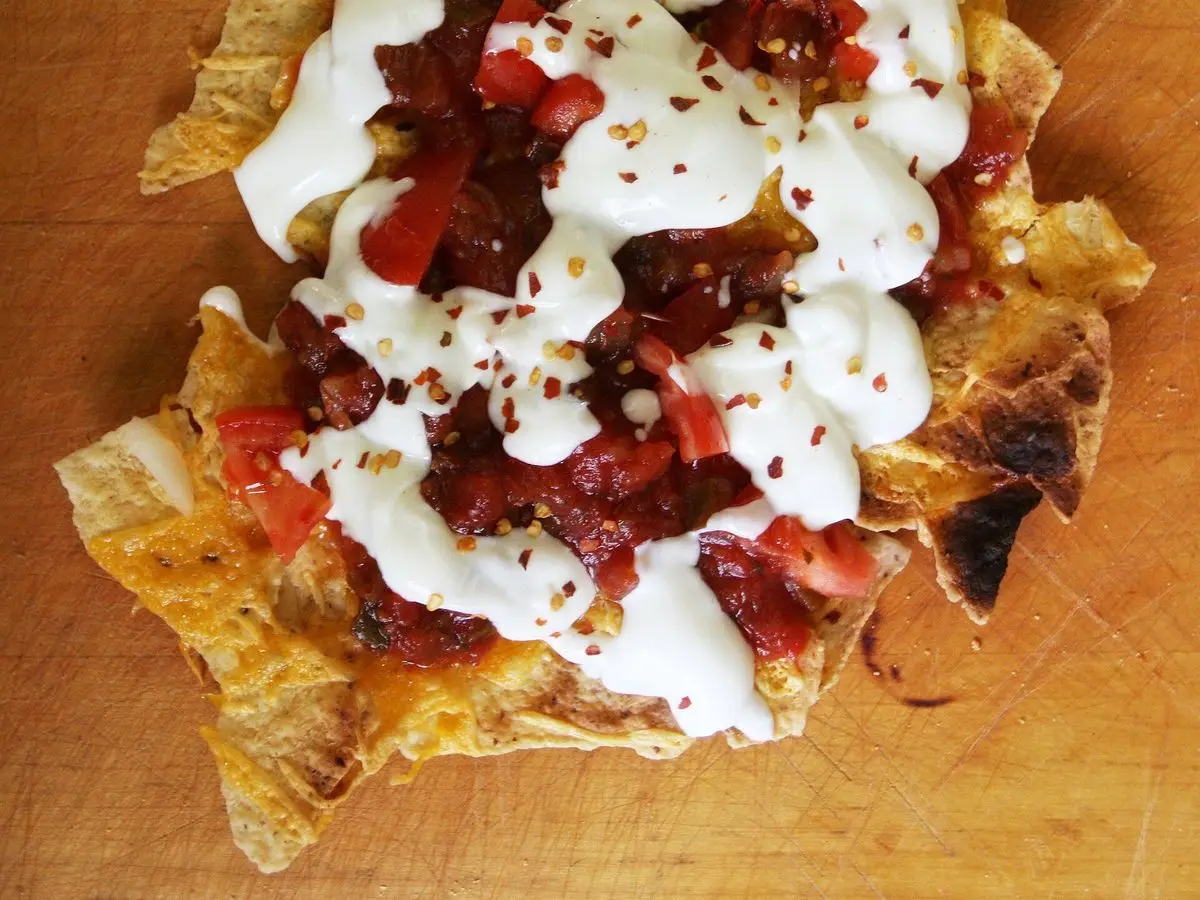 Nachos con chili de carne, nata agria y queso sobre una tabla de madera
