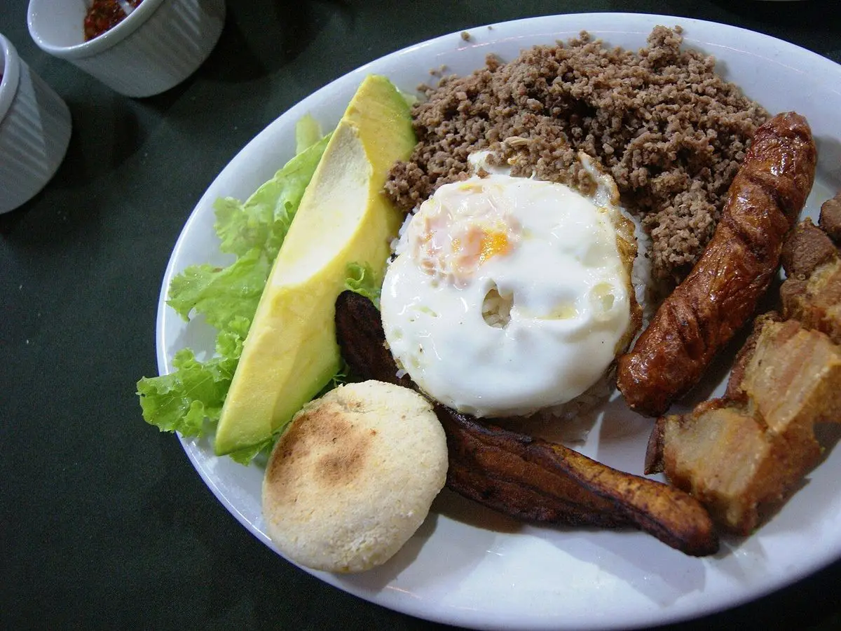 Bandeja paisa con carne molida, huevo frito, aguacate, arepa, chorizo y chicharrón en un plato blanco