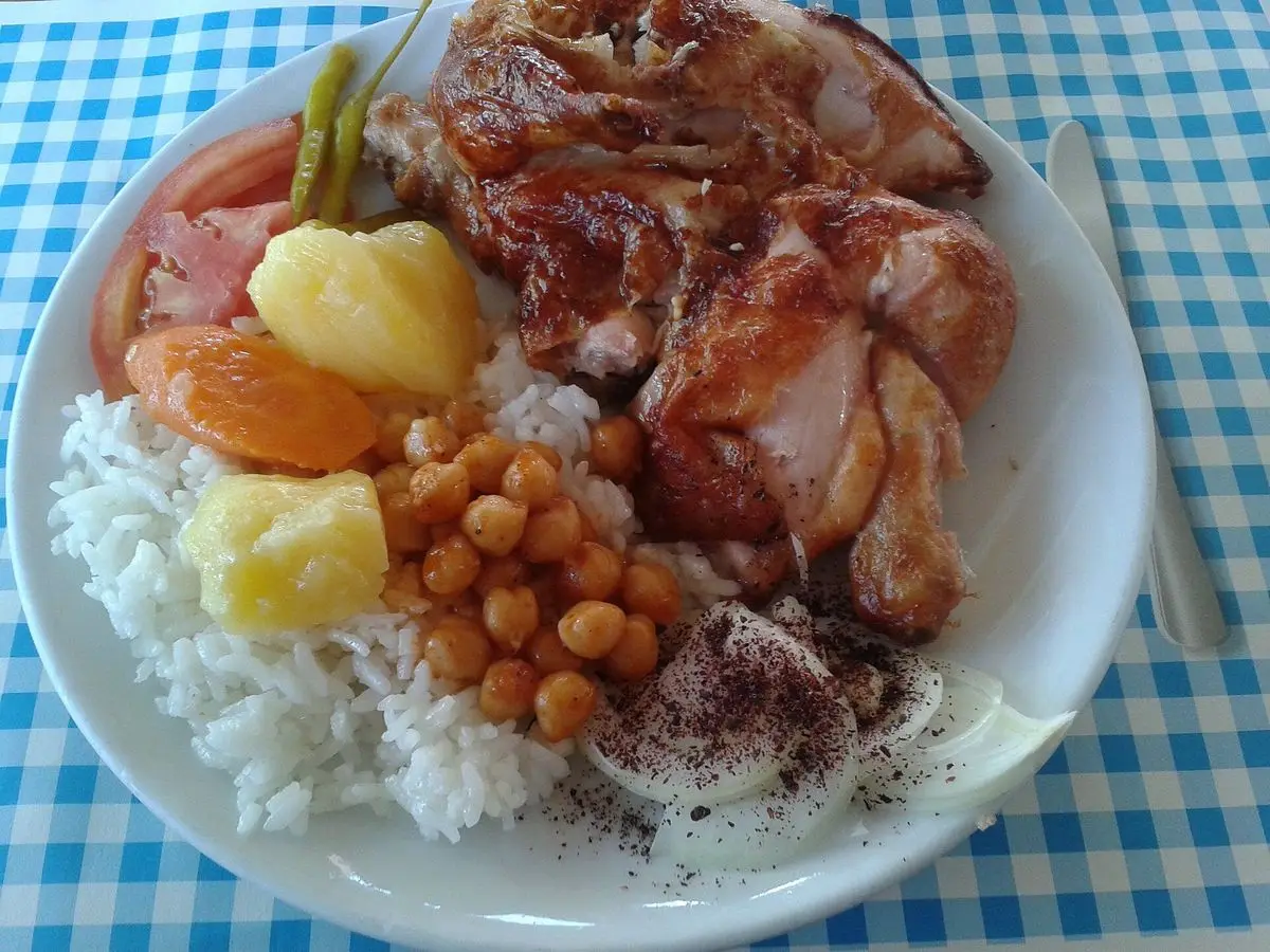 Plato con pollo asado, arroz blanco, garbanzos y rodajas de naranja y piña sobre mantel de cuadros