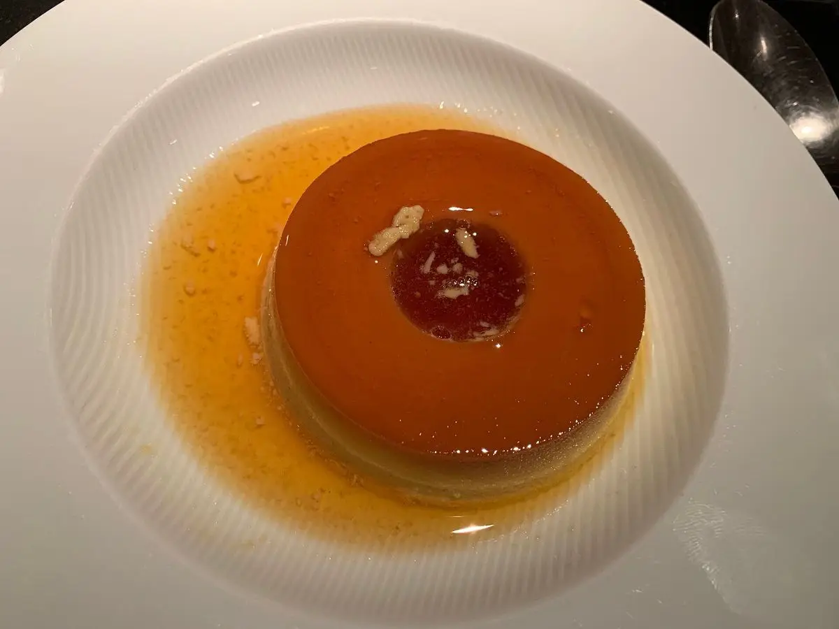 Flan con caramelo oscuro desmoldado sobre un plato blanco con salsa de caramelo alrededor