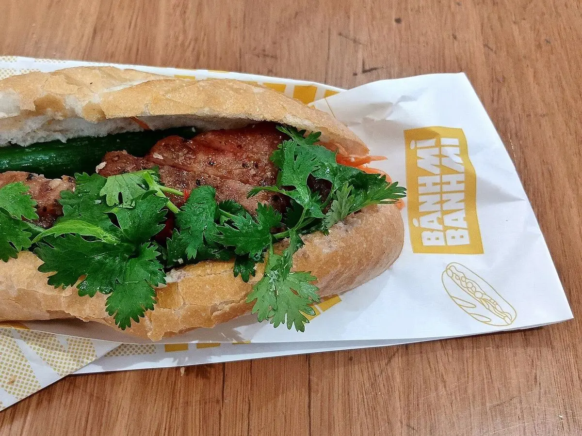 Bocadillo vietnamita en baguette con carne asada y abundante cilantro fresco sobre papel