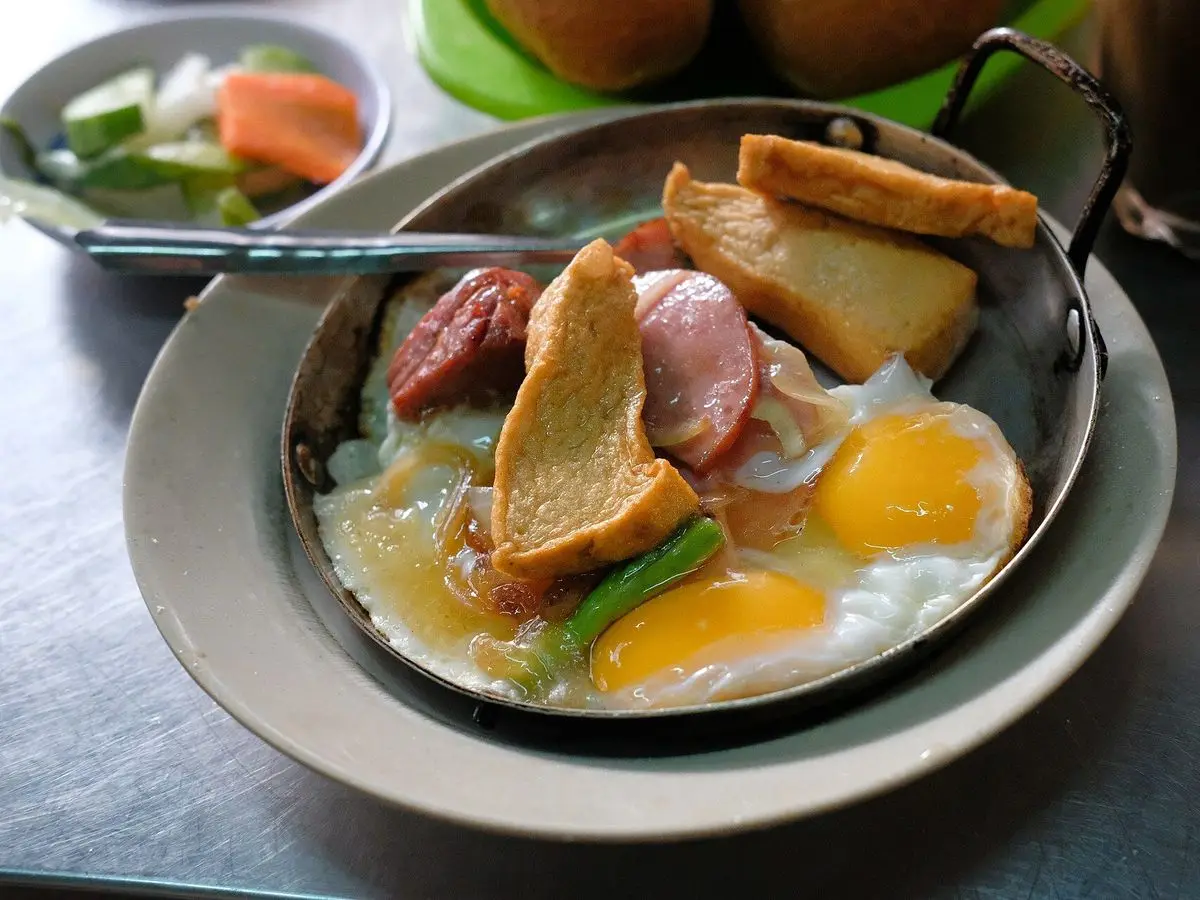 Sartén de hierro con huevos fritos, embutido y pan crujiente servida sobre un plato