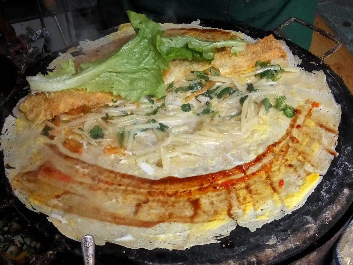 Crepe fina abierta sobre la plancha con huevo, cebolleta, cilantro, hilos de salsa picante y una hoja de lechuga