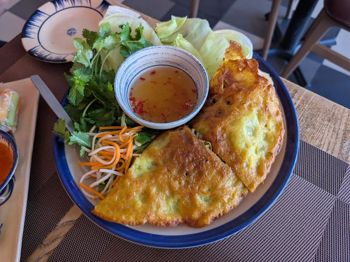 Crepes vietnamita dorada junto a hierbas frescas, lechuga y salsa para mojar en un plato