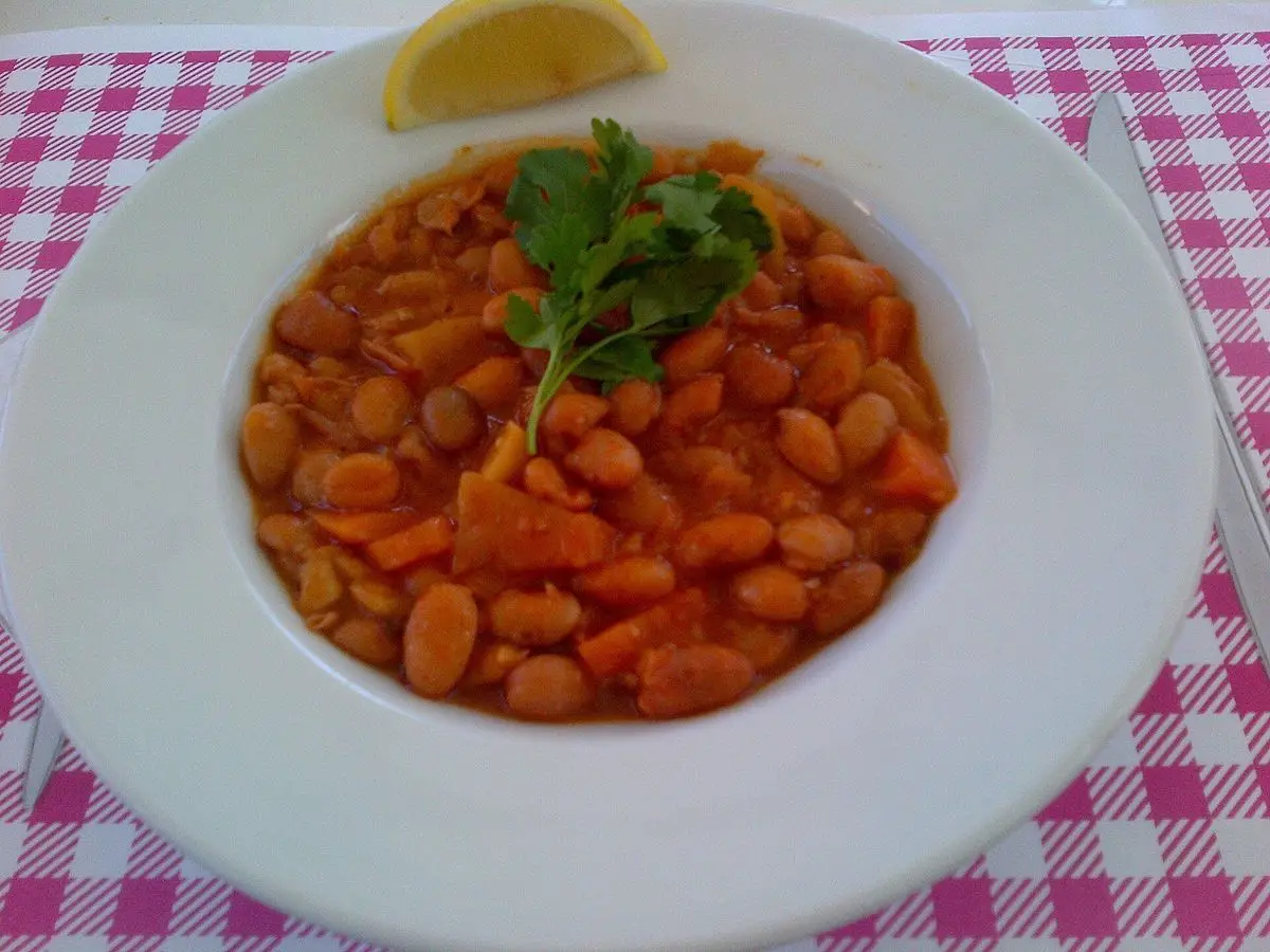 Plato blanco de alubias pintas guisadas con zanahoria, perejil y limón sobre mantel de cuadros