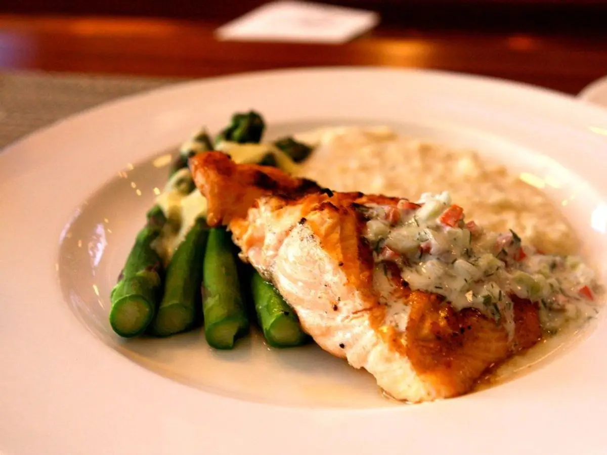 Lomo de salmón dorado con salsa de hierbas y espárragos verdes sobre puré, en un plato blanco