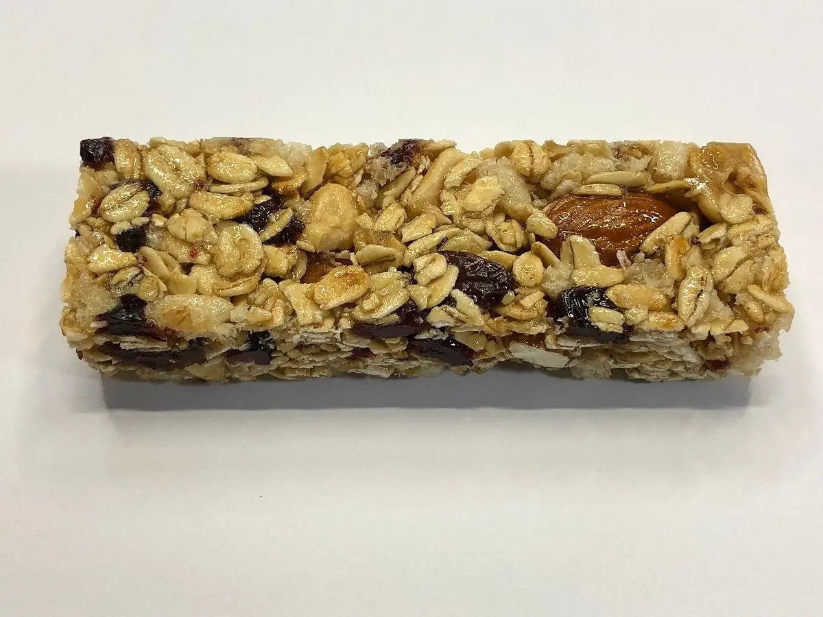 Barrita de granola con copos de avena, frutos secos y pasas sobre fondo blanco