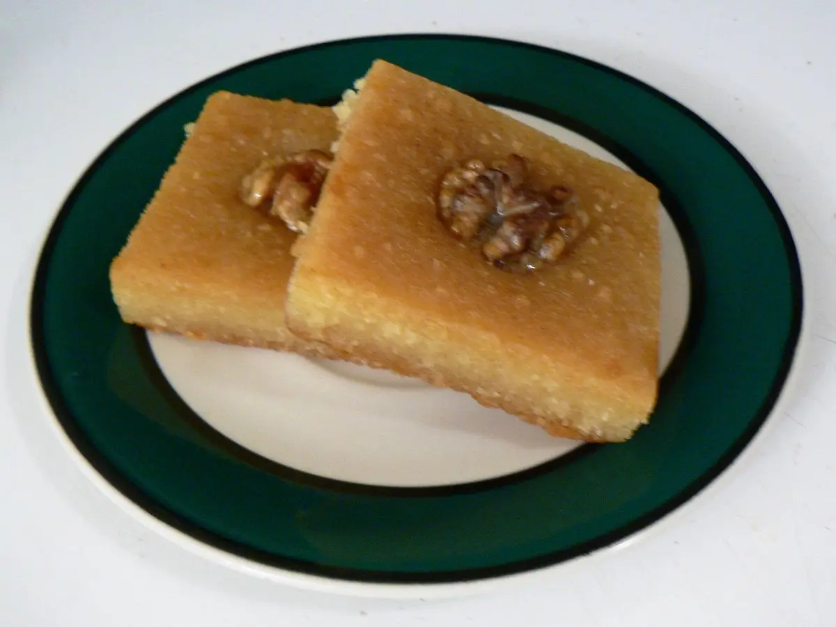 Dos porciones de basbousa dorada de sémola con una almendra encima sobre un plato blanco