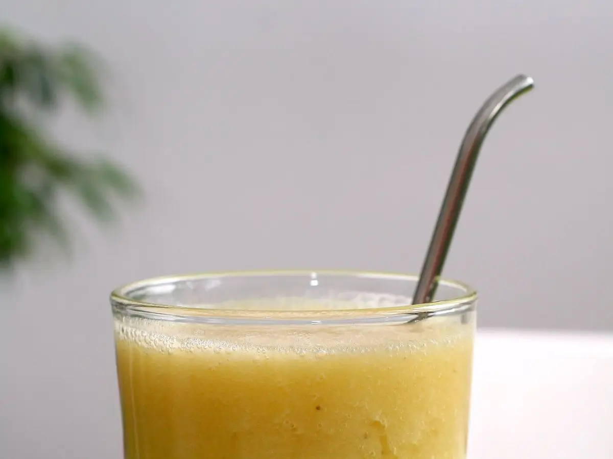 Vaso alto de batido amarillo cremoso con una pajita sobre una mesa