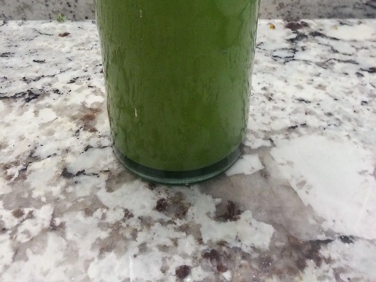 Vaso de batido verde cremoso sobre una encimera de granito