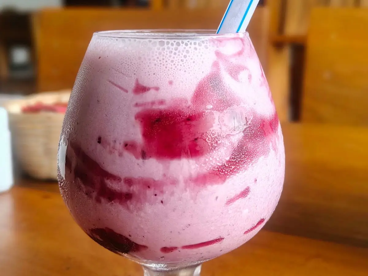 Batido rosa de frutos rojos con vetas moradas en una copa de cristal con pajita