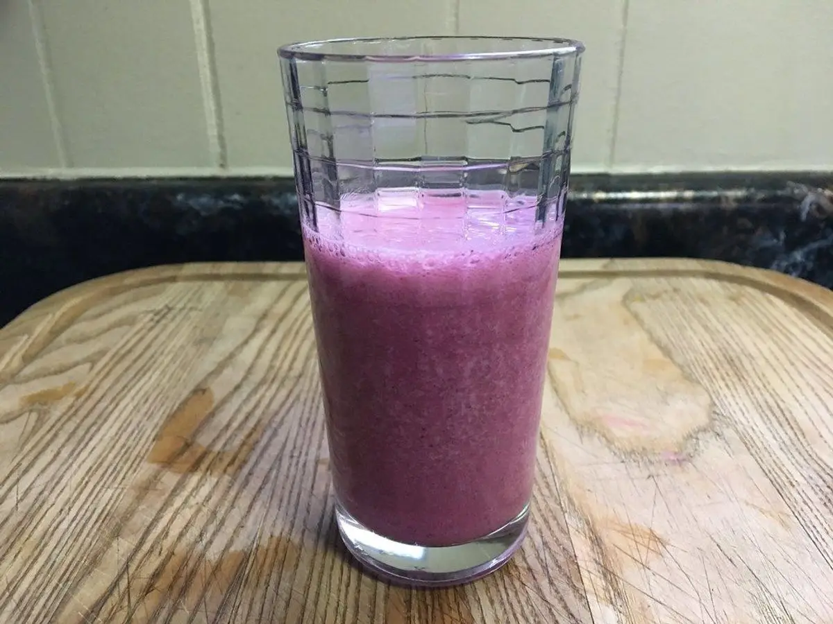 Vaso alto de batido espeso de color rosa violáceo sobre una tabla de madera