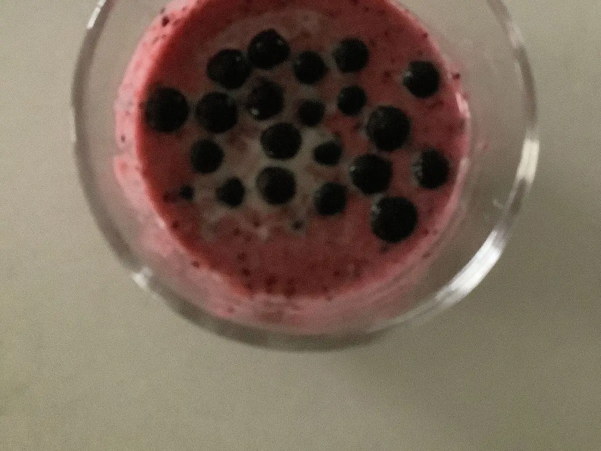 Vaso de cristal con batido morado oscuro con arándanos negros por encima visto desde arriba
