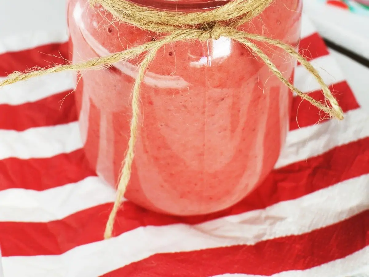 Tarro de cristal con batido rosa de frutos rojos, pajita de rayas y cinta de cordel