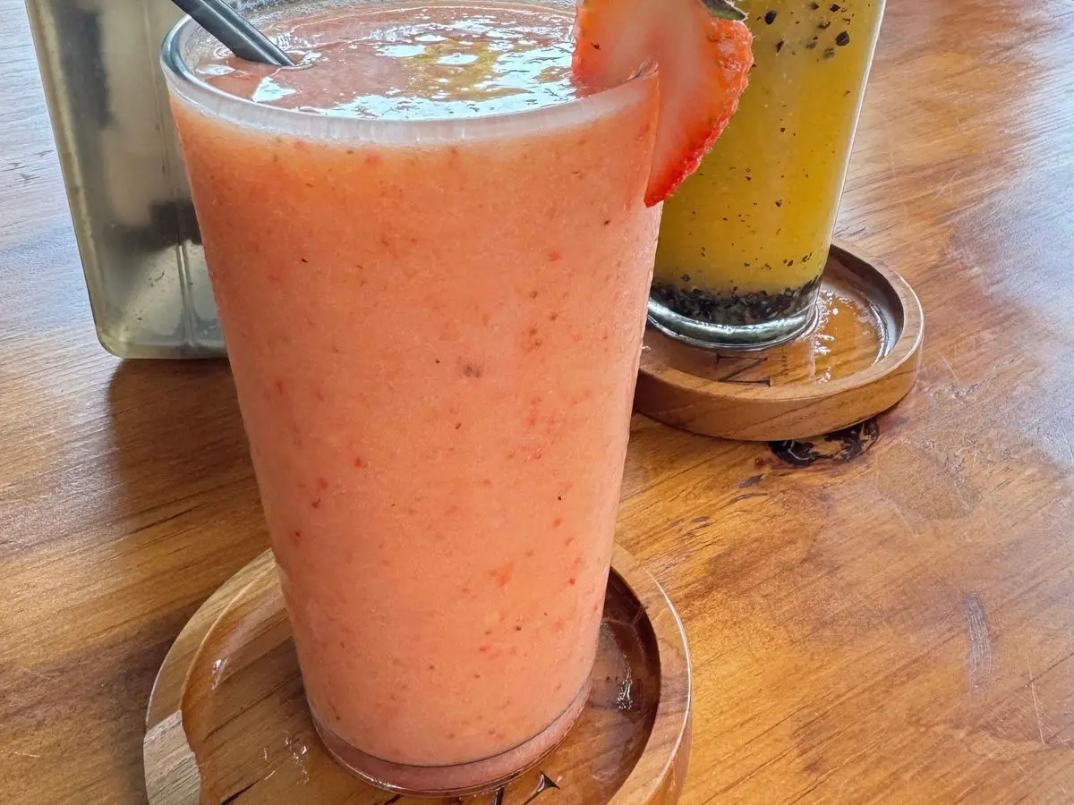 Batido rosado de fresa en un vaso alto con una rodaja de fresa en el borde