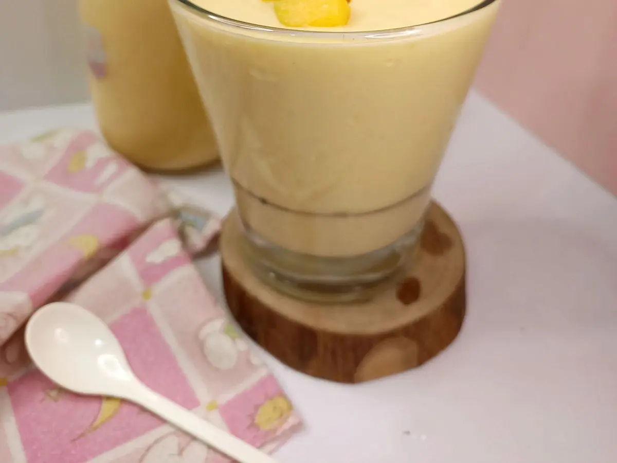 Vaso de batido cremoso de mango con trocitos de mango encima y una pajita rosa