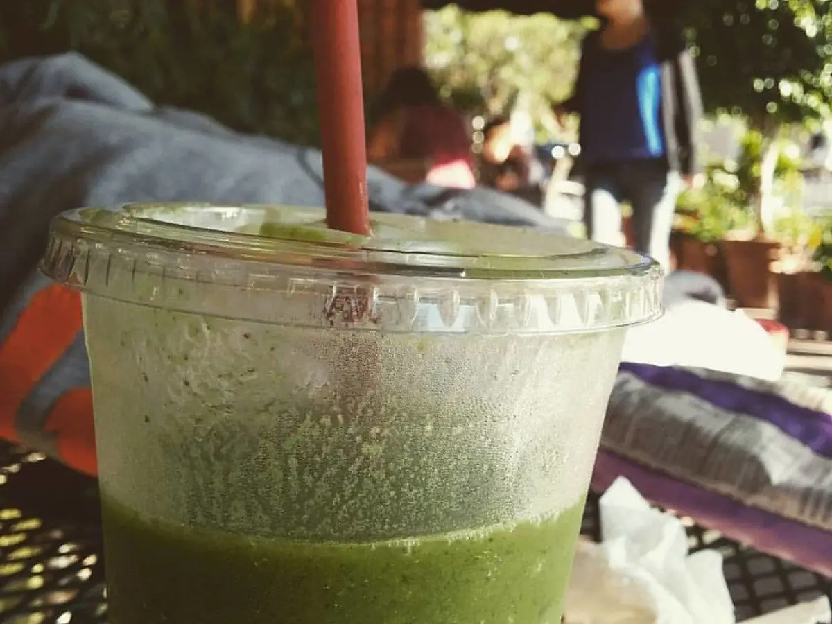 Vaso de plástico con batido verde espeso y una pajita roja en una mesa de terraza