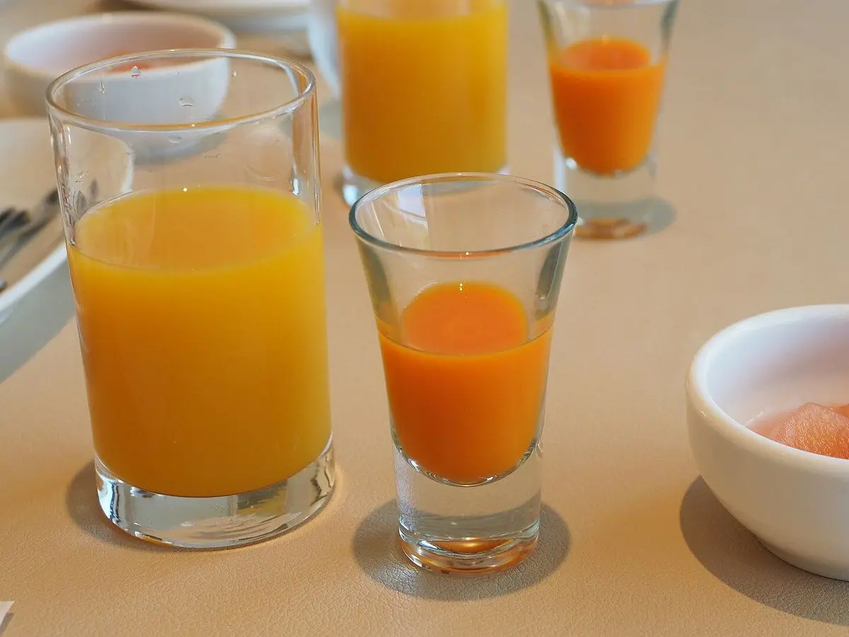 Vasos de zumo de naranja y batido anaranjado de zanahoria junto a un cuenco con fruta