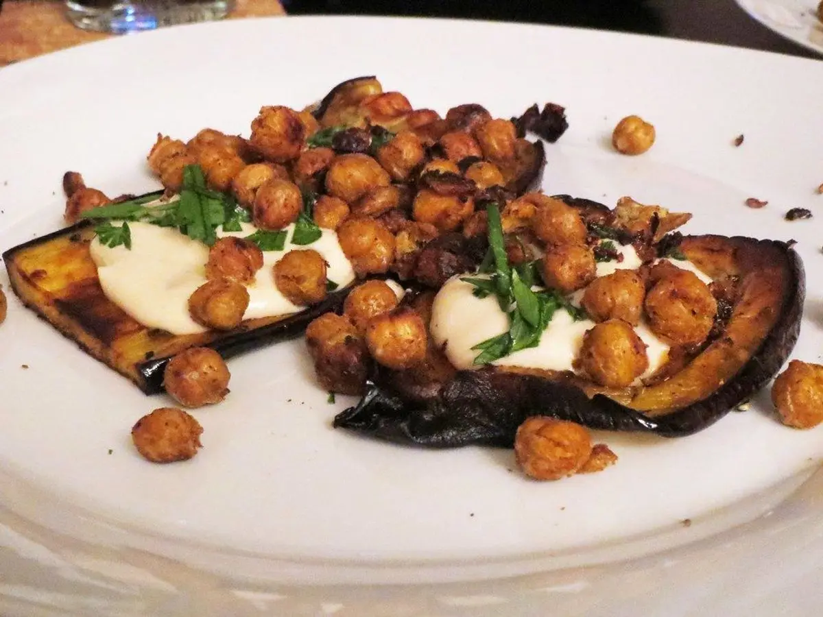 Berenjenas asadas con salsa cremosa de yogur, garbanzos crujientes y hierbas frescas en un plato blanco