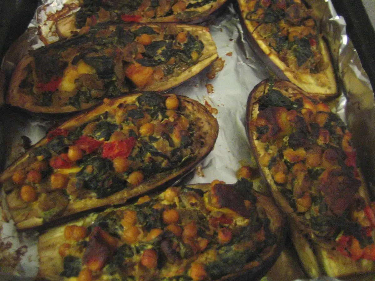 Berenjenas abiertas y rellenas de verduras y legumbres, asadas sobre una bandeja con papel de aluminio