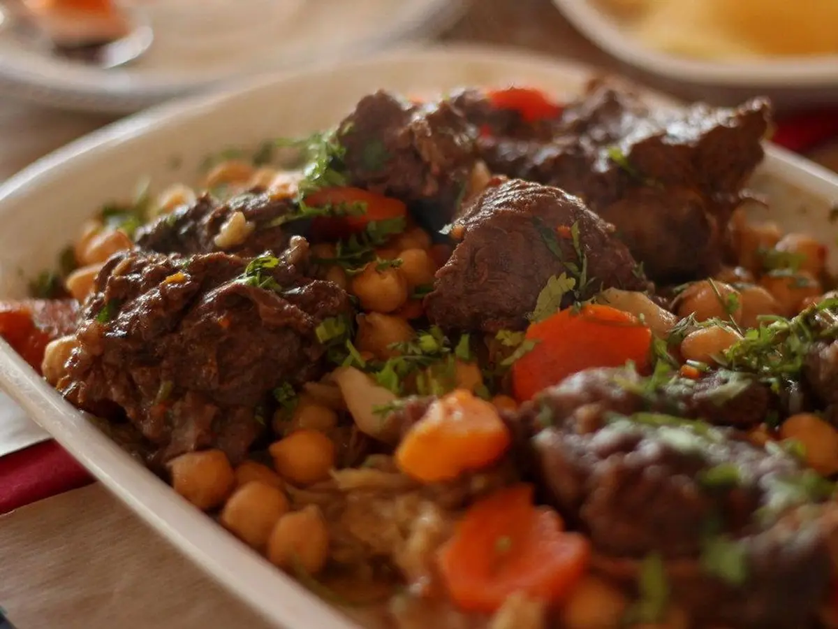 Guiso de carne con garbanzos, zanahoria y perejil en una fuente blanca