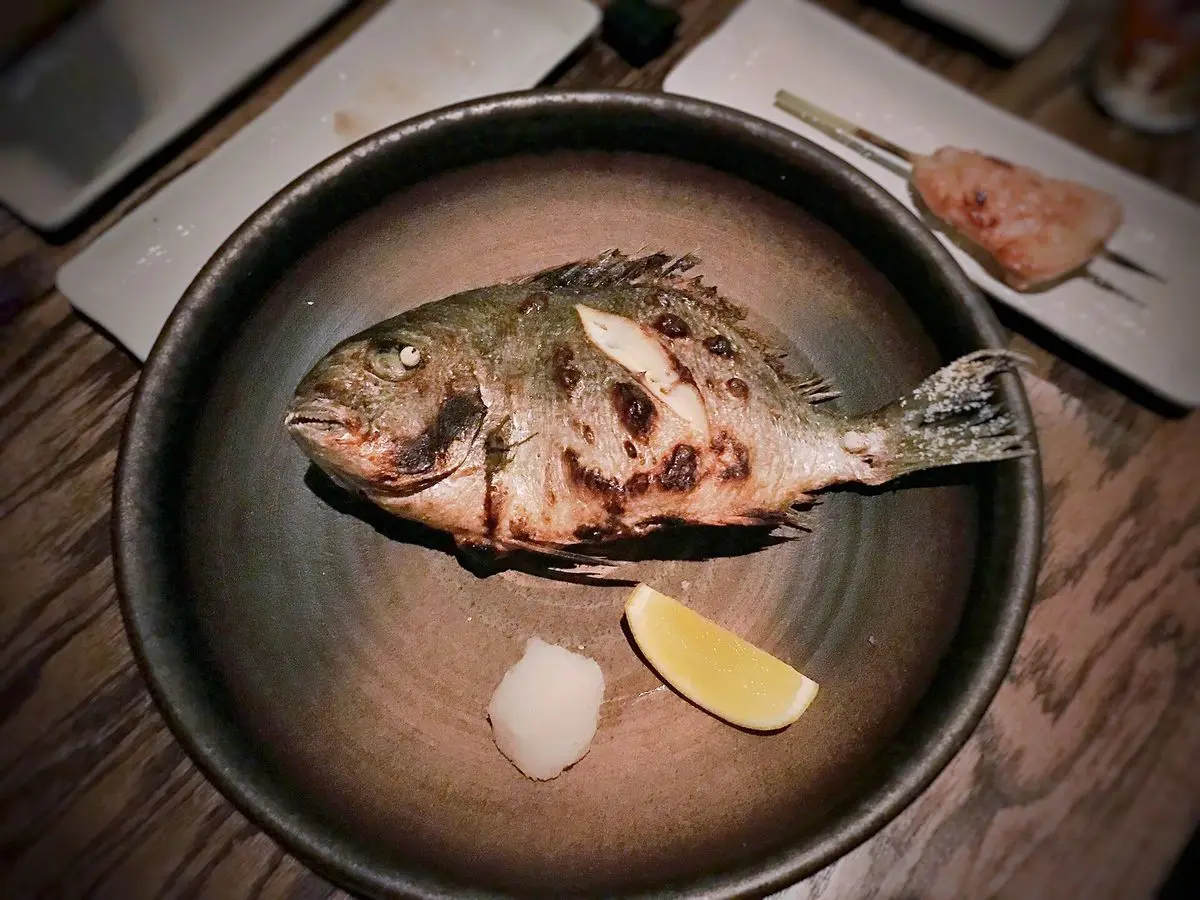 Besugo entero a la plancha con una cuña de limón sobre un plato hondo oscuro