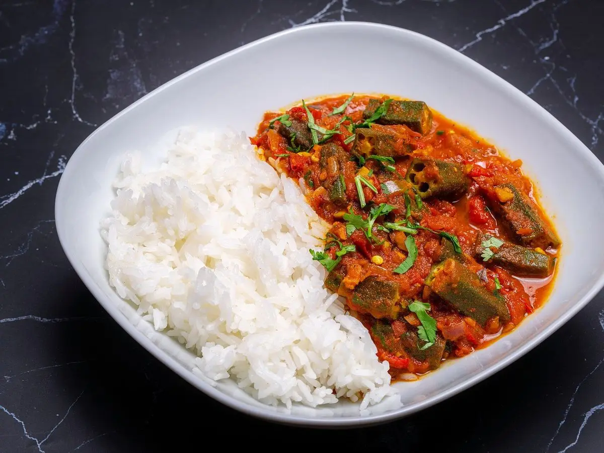Plato blanco con arroz blanco y okra guisada con tomate y especias sobre una mesa oscura