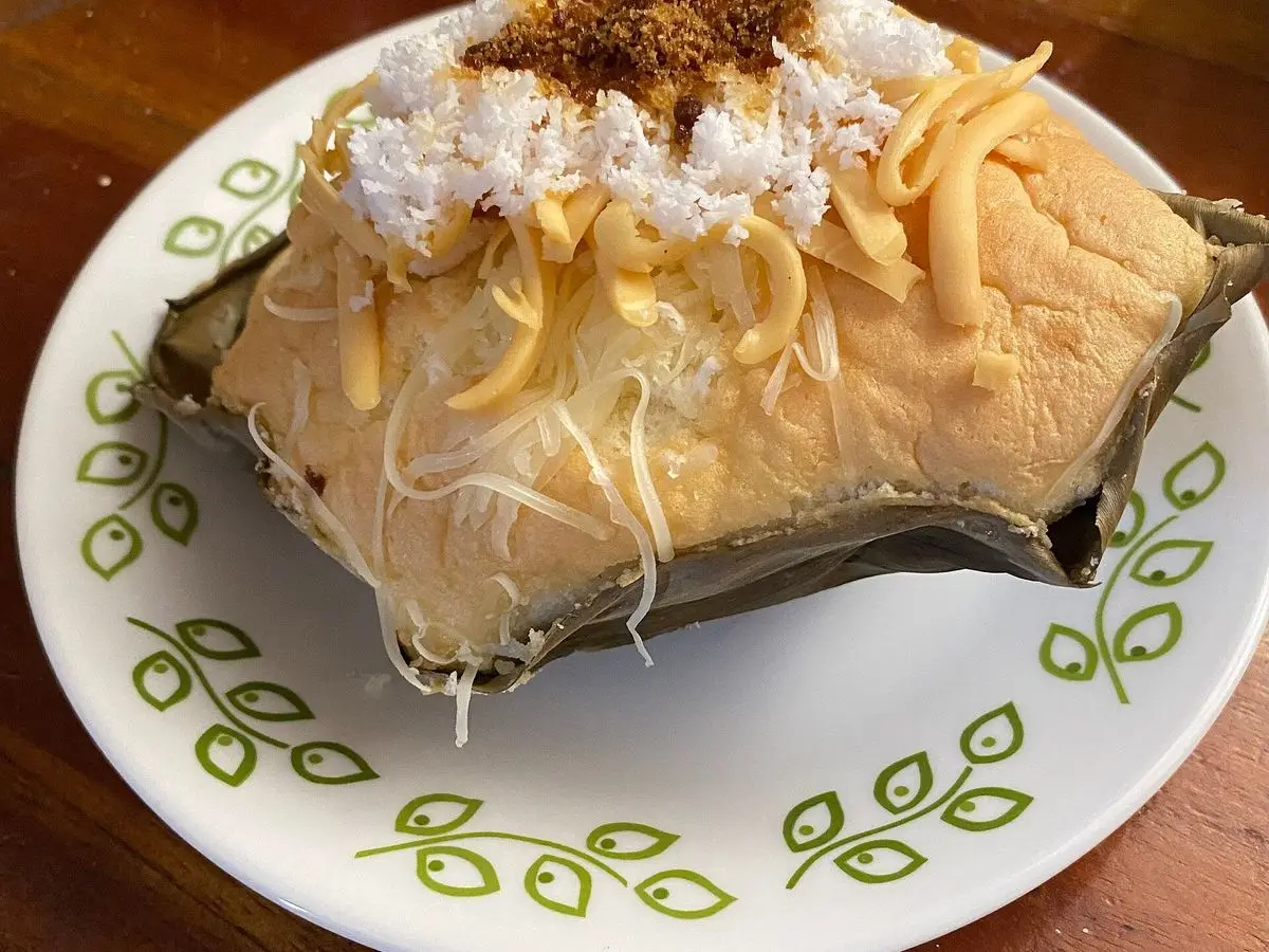 Bibingka, pastel de arroz y coco cocido en hoja de plátano con queso, huevo salado y coco rallado por encima
