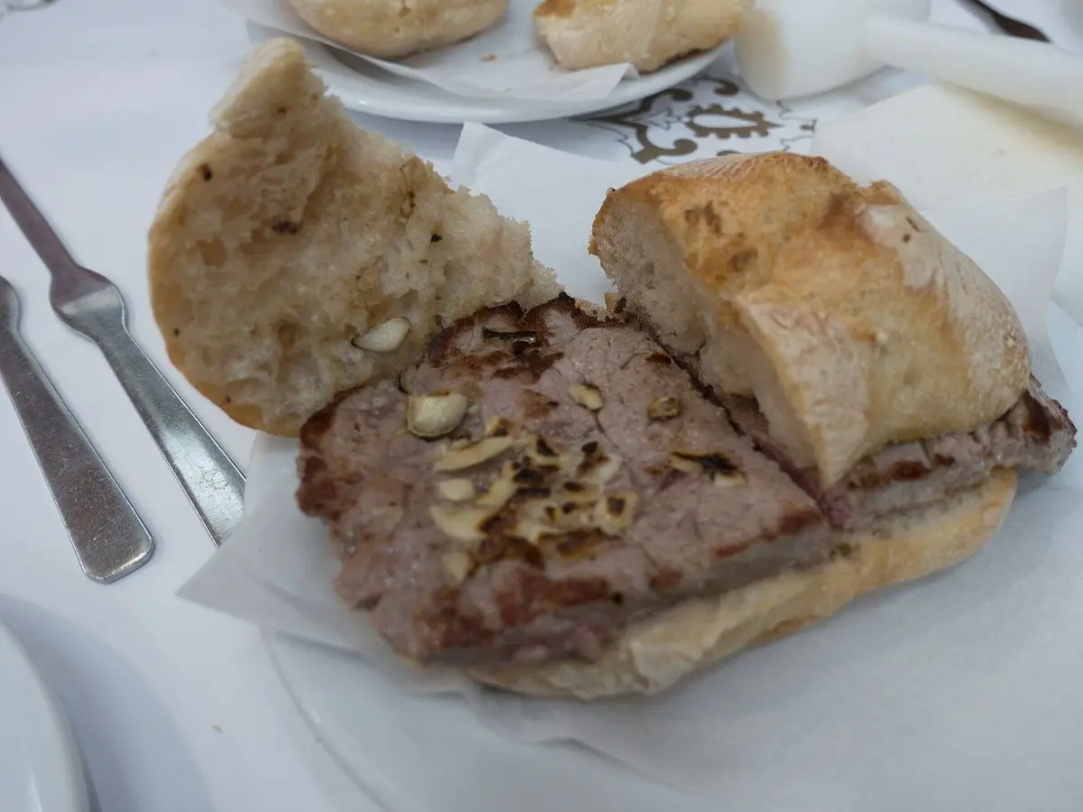 Bocadillo portugués de carne de cerdo en pan crujiente abierto sobre un plato blanco