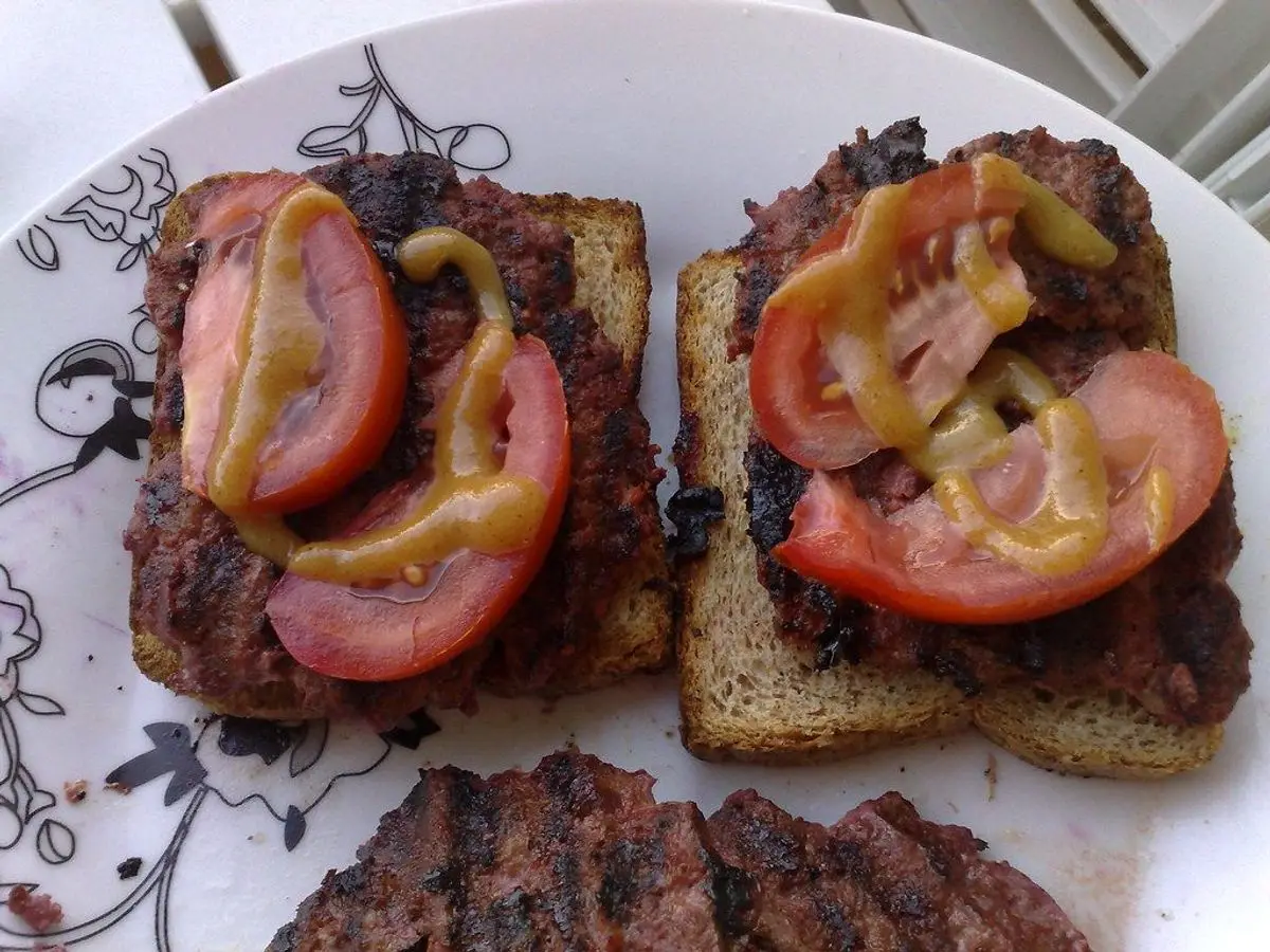 Dos hamburguesas de ternera sobre pan de centeno con rodajas de tomate y mostaza en un plato