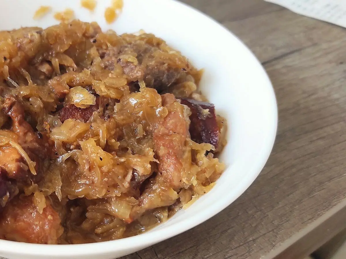 Cuenco blanco de bigos polaco con col fermentada y trozos de carne de cerdo y salchicha