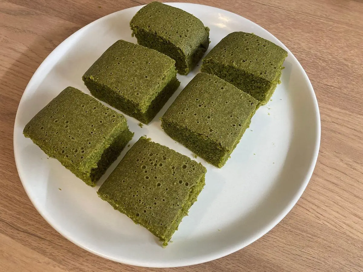 Plato blanco con cuadrados de bizcocho verde de té matcha sobre una mesa de madera