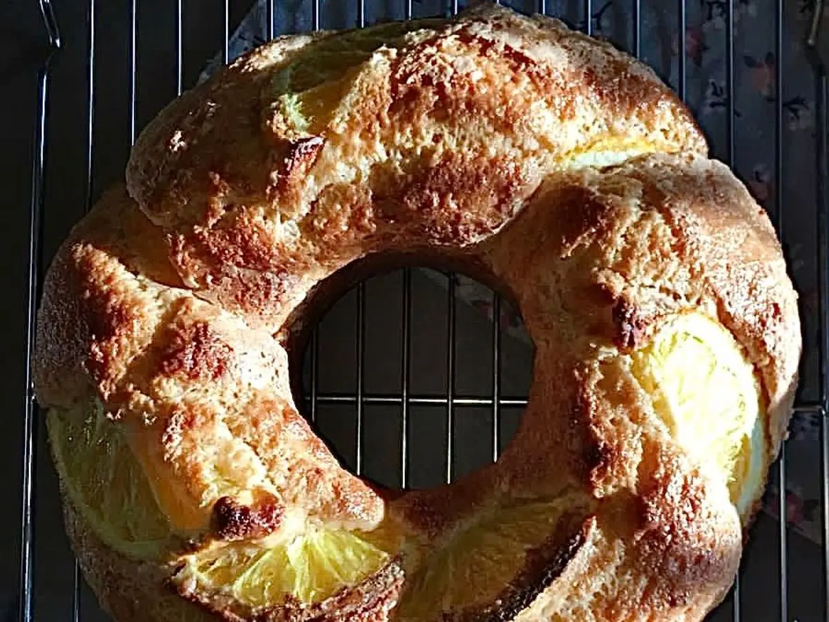 Bizcocho en forma de rosca decorado con rodajas de naranja sobre una rejilla con ramitas de romero