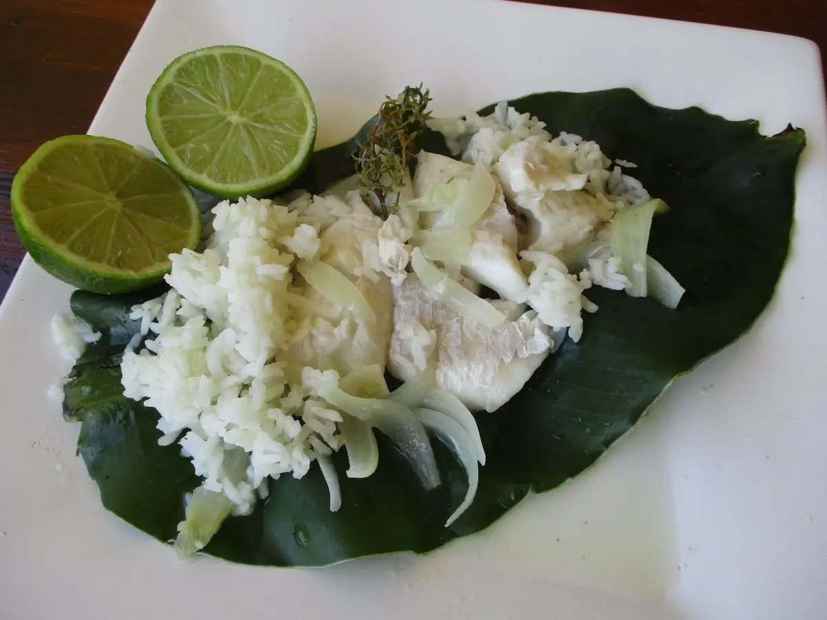 Pescado blanco escalfado con cebolla y media lima sobre una hoja verde en un plato blanco