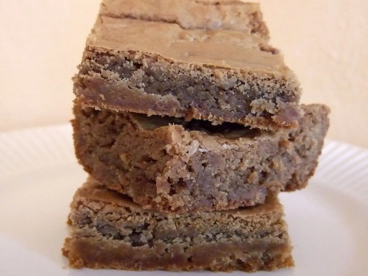 Tres cuadrados de blondie apilados, de color caramelo, sobre un plato blanco