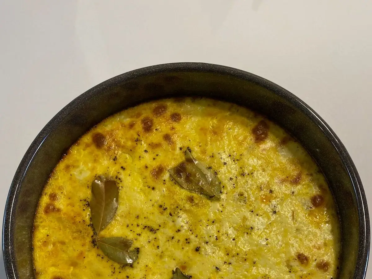 Bobotie al horno con cobertura dorada de huevo y hojas de laurel en una fuente negra