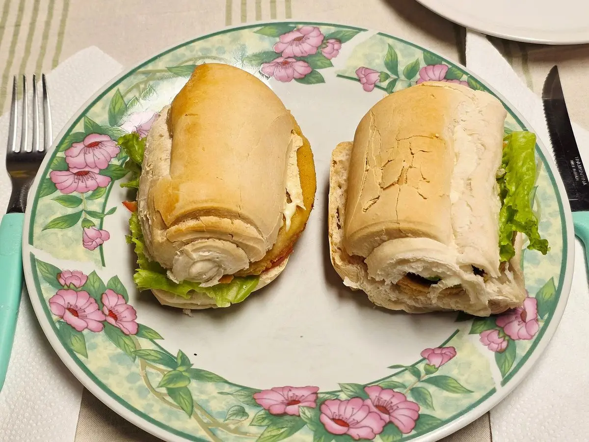 Dos bocadillos de pescado empanado con lechuga y tomate en pan alargado sobre un plato decorado con flores