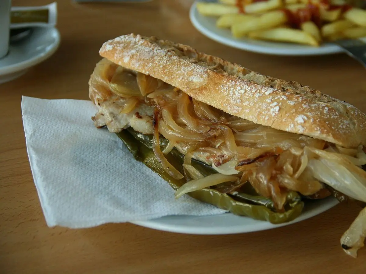 Bocadillo de lomo con cebolla pochada y pimientos verdes en un plato con patatas fritas