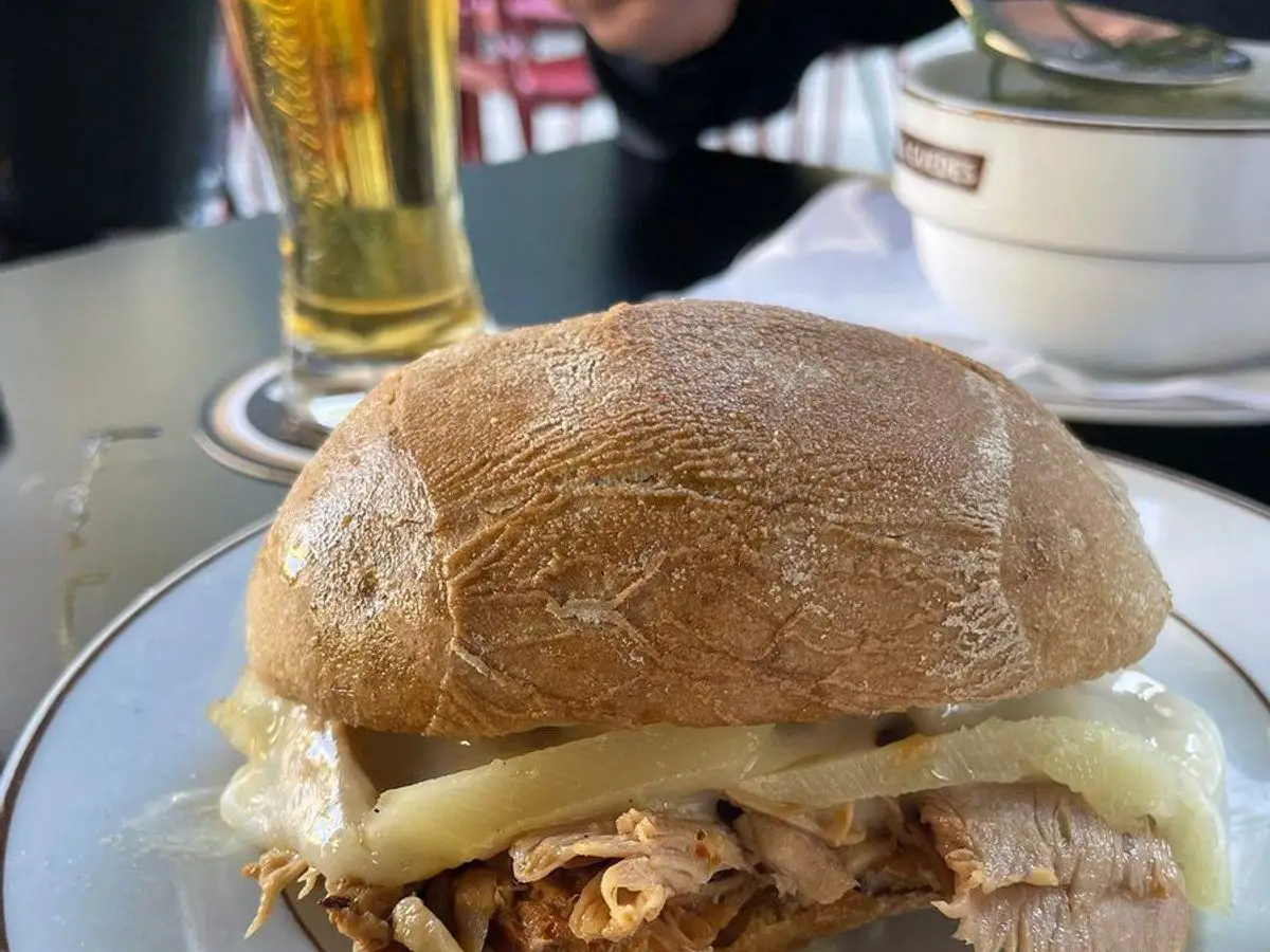 Bocadillo de pan crujiente con lomo de cerdo y queso fundido sobre un plato blanco