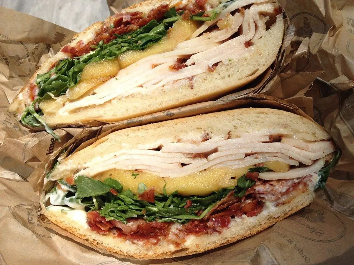 Dos mitades de bocadillo de pavo en lonchas con rúcula y queso sobre papel de estraza