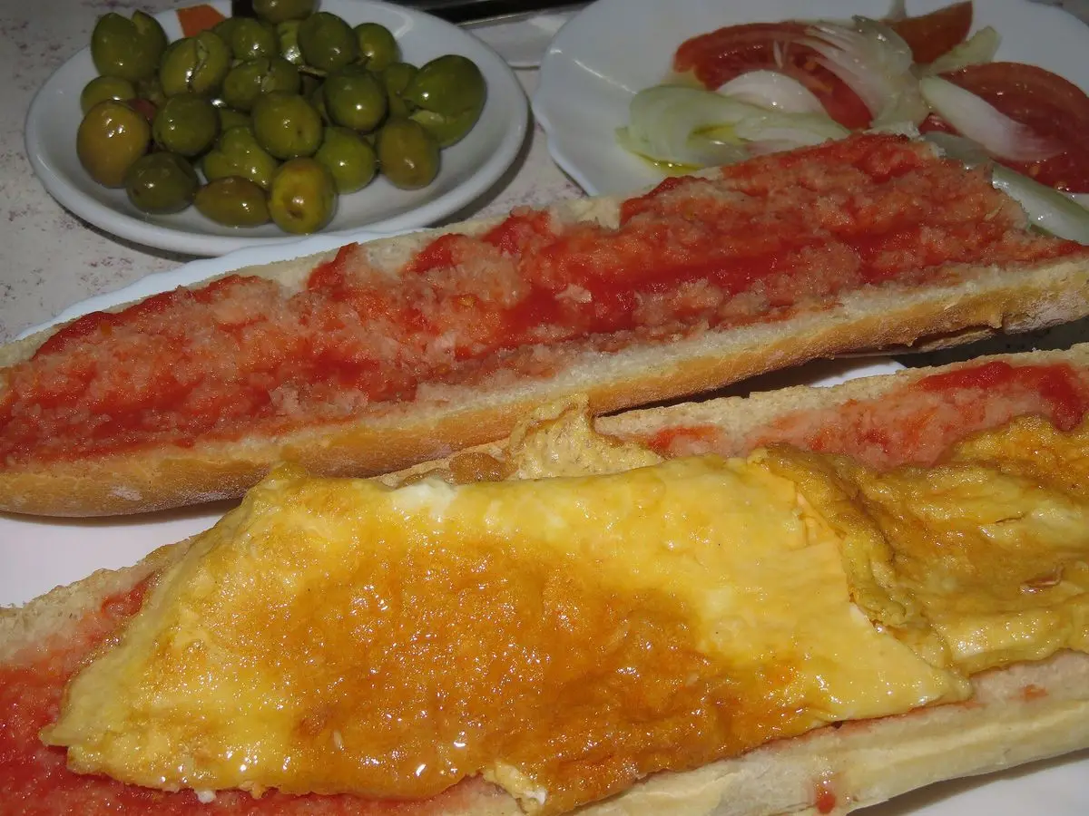Bocadillo de tortilla francesa con pan restregado de tomate y un platito de aceitunas verdes