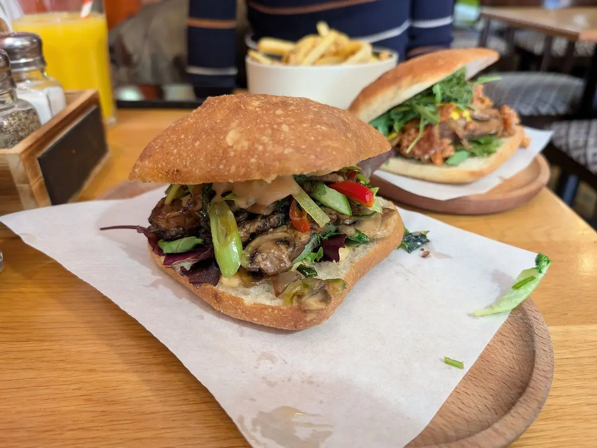 Bocadillo en pan rústico con tempeh frito y verduras frescas sobre papel en una mesa de madera