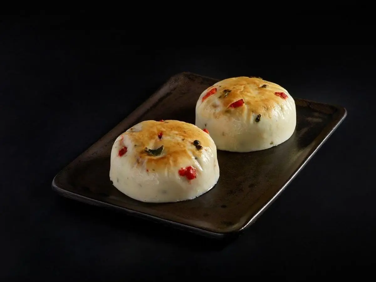 Dos bocaditos de huevo al vapor con trocitos de pimiento rojo sobre una bandeja oscura