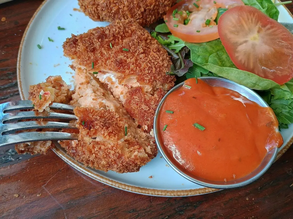 Bocados de pescado rebozados y crujientes con ensalada de tomate y lechuga y un cuenco de salsa roja