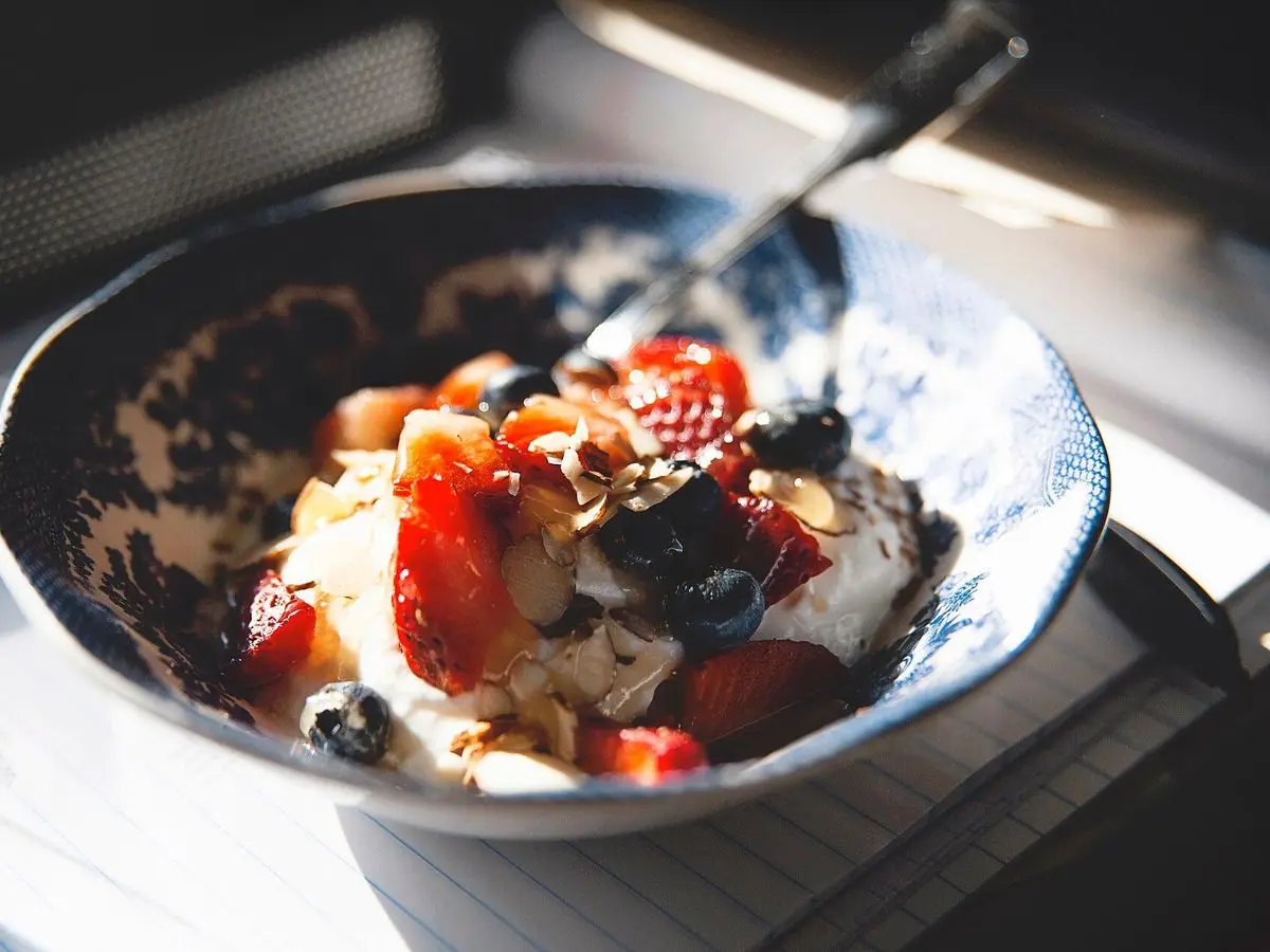 Bol con crema blanca, fresas y frutos rojos frescos con una cuchara a la luz de una ventana