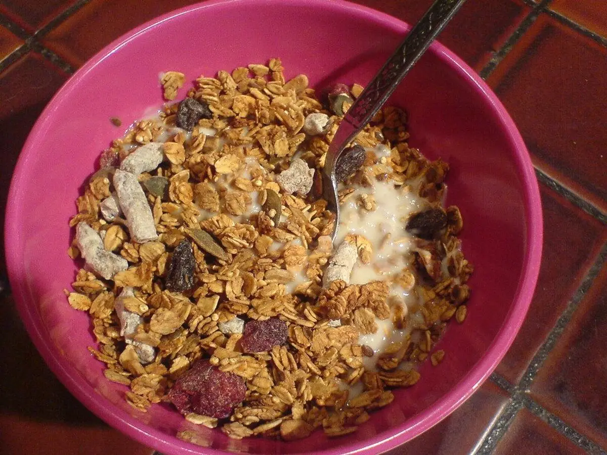 Cuenco rosa de granola con frutos secos y copos con una cuchara