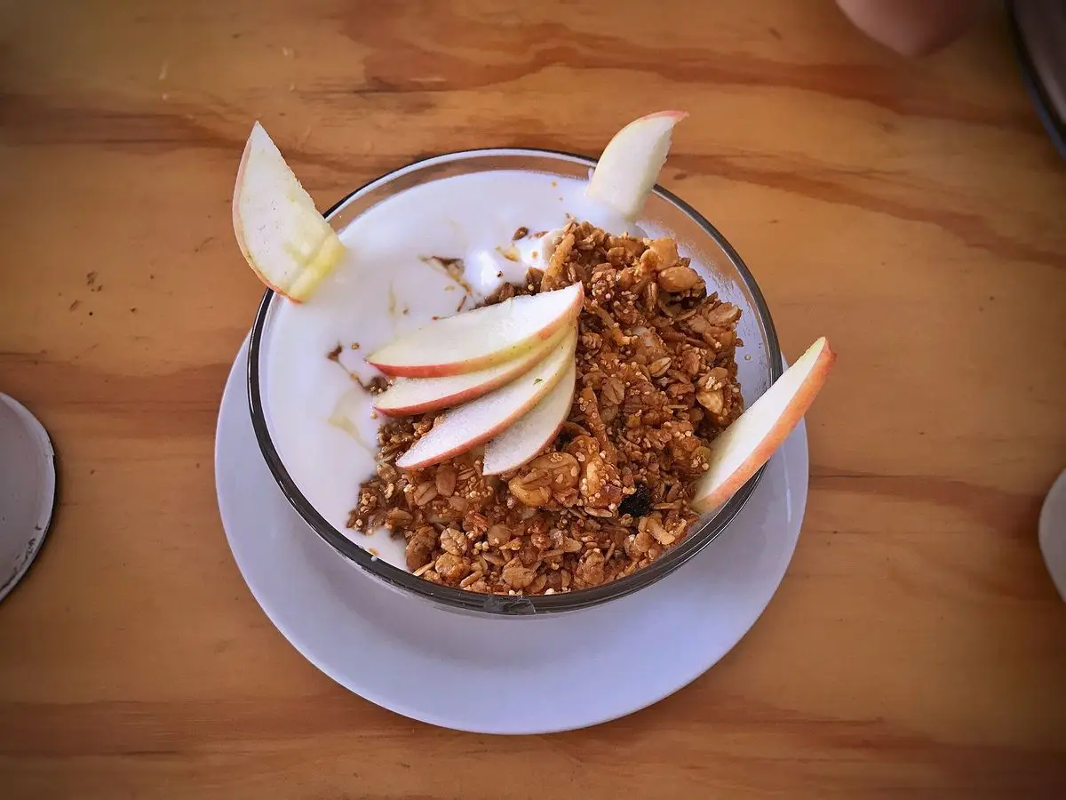 Vaso de yogur con granola dorada y rodajas de manzana o pera sobre un plato blanco